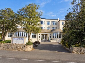 A hotel with a sign reading 'Trecarn Hotel,' a paved entrance, and a stone wall with greenery. - The Trecarn Hotel (Torquay)