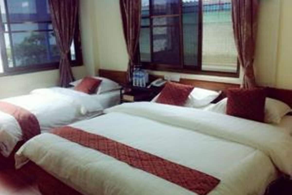 Habitación de hotel con dos camas, cada una con ropa de cama blanca y detalles en rojo, un cabecero de madera y una ventana con cortinas.