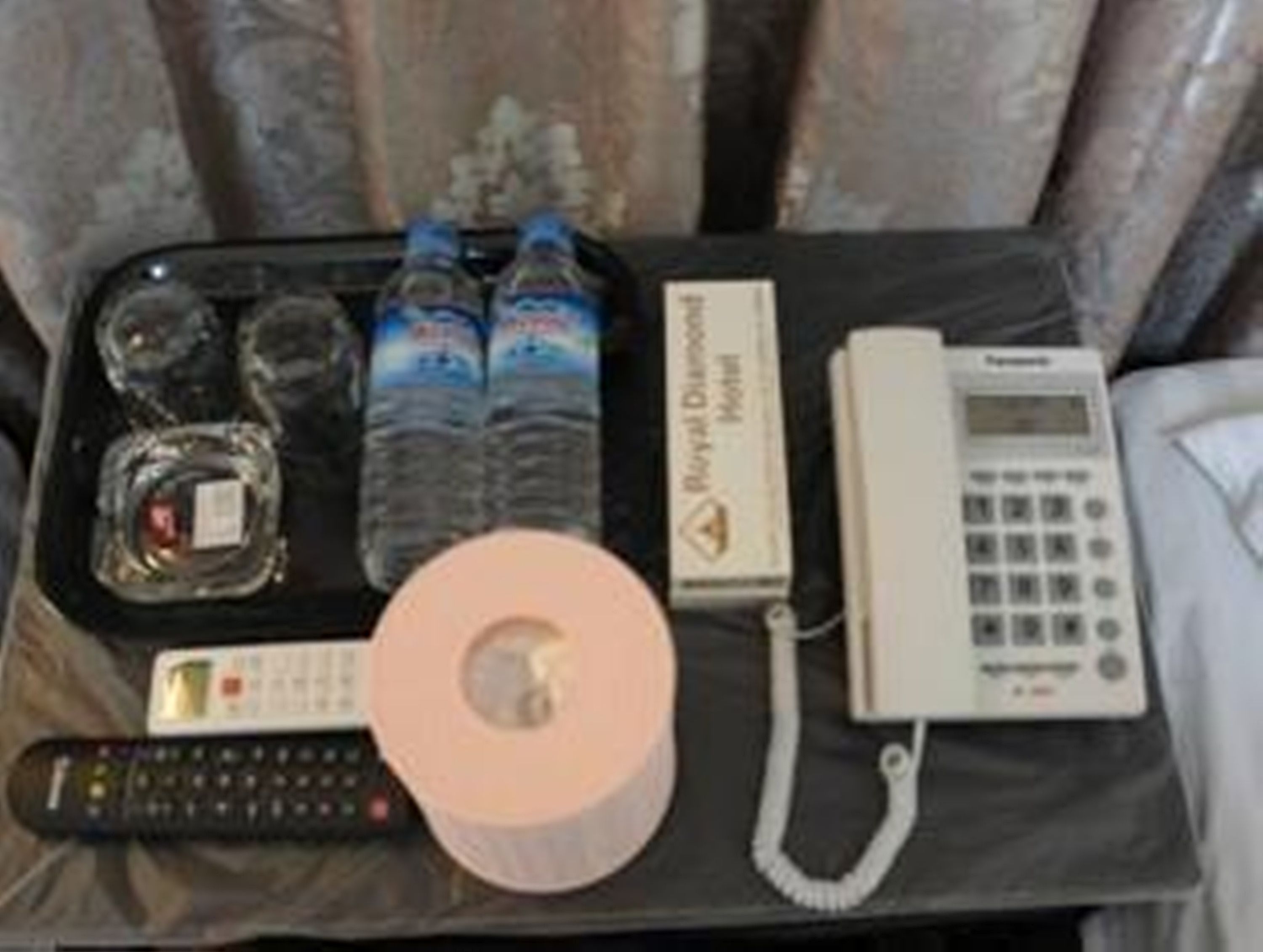 A tray with bottled water, a remote control, a phone, and a roll of toilet paper.