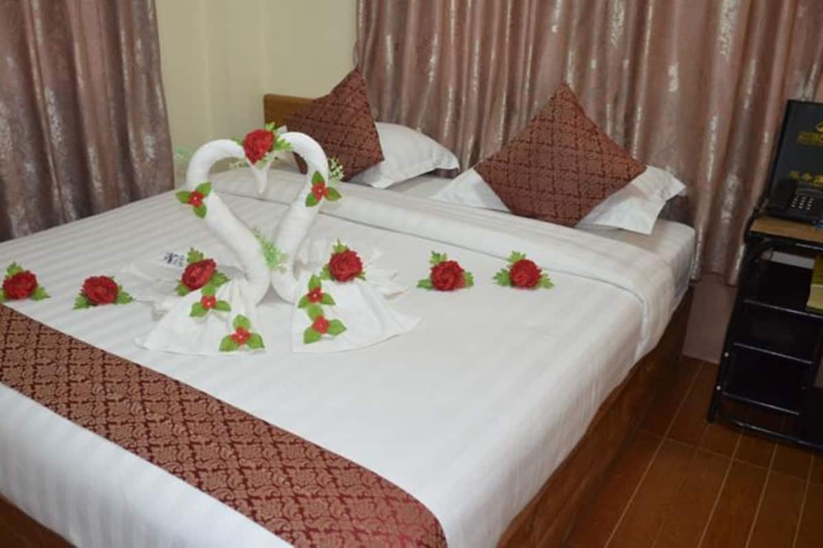 Una cama bien hecha con sábanas blancas, una colcha de cuadros en rojo y marrón, y rosas rojas y cisnes blancos decorativos sobre la cama.