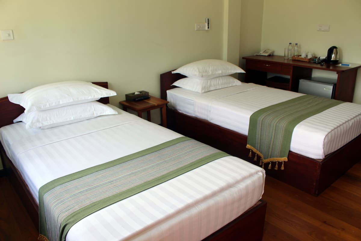 A hotel room with two single beds, a small desk, and a mini-fridge.