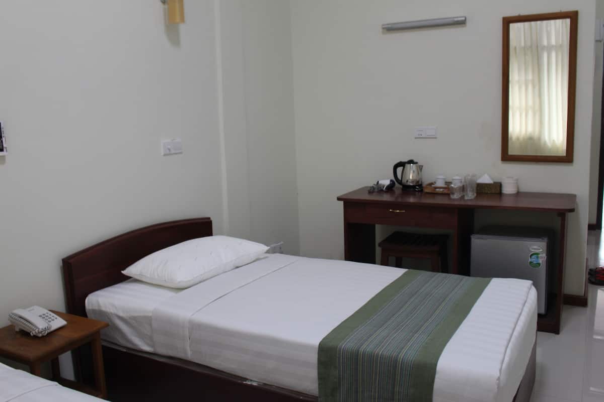 A hotel room with a single bed, a small desk with a refrigerator, a telephone, and a mirror on the wall.