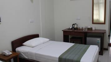 A hotel room with a single bed, a small desk with a refrigerator, a telephone, and a mirror on the wall.
