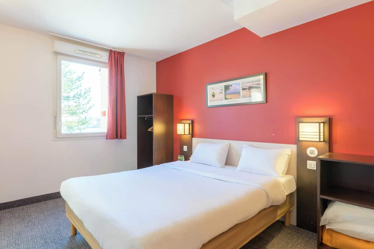 Una habitación de hotel con una cama grande, una ventana con cortinas, una pared roja y dos lámparas de noche.