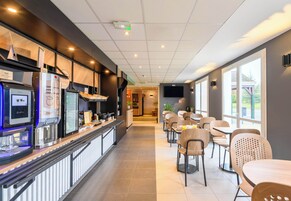 Un café moderno con una barra larga, zona de estar y amplios ventanales.