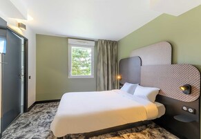 Habitación de hotel con cama, ventana con cortinas, luz empotrada en la pared y puerta.