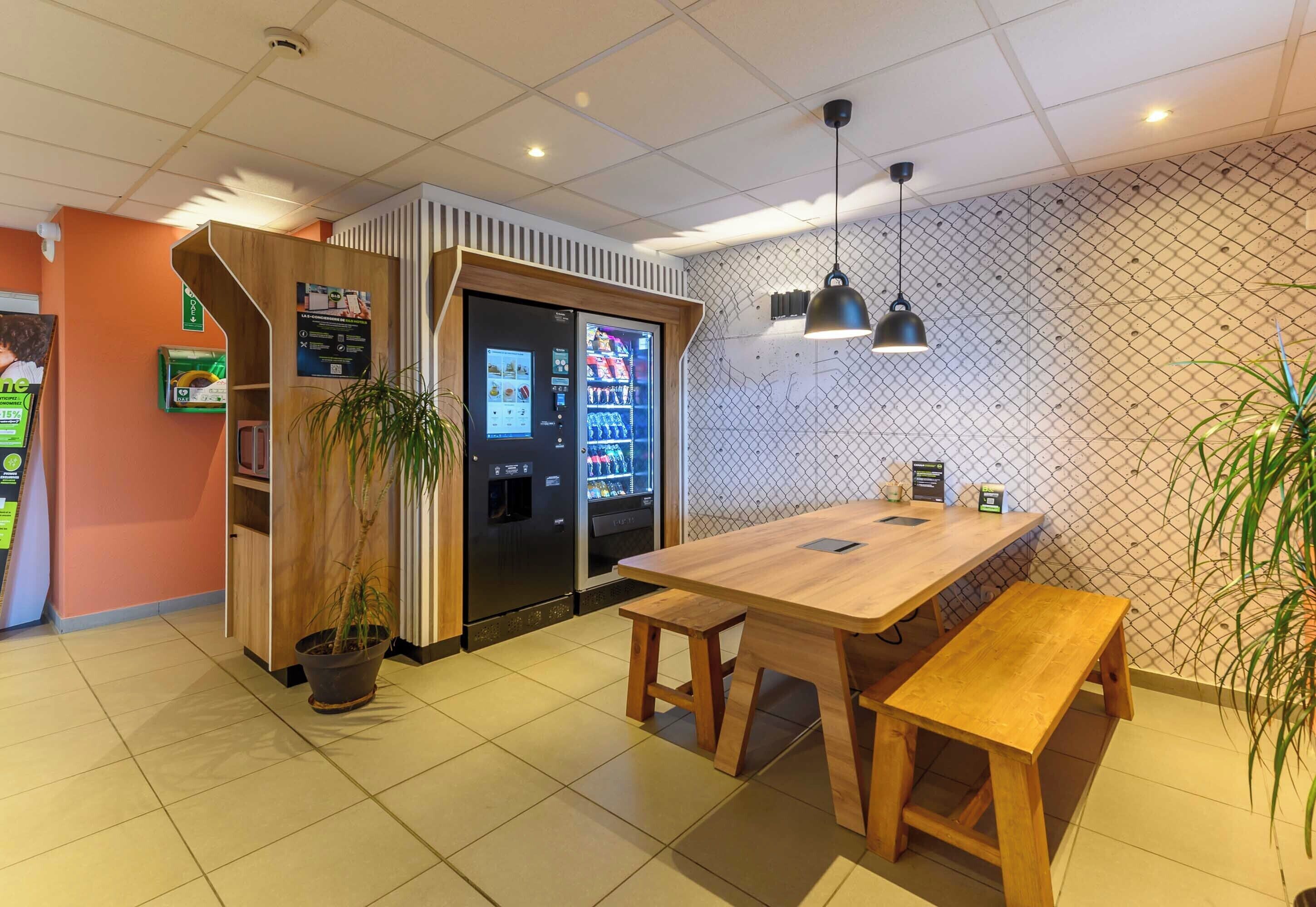 Ein Restaurant mit Holztischen und Bänken, einem Automaten und einem Blumentopf.