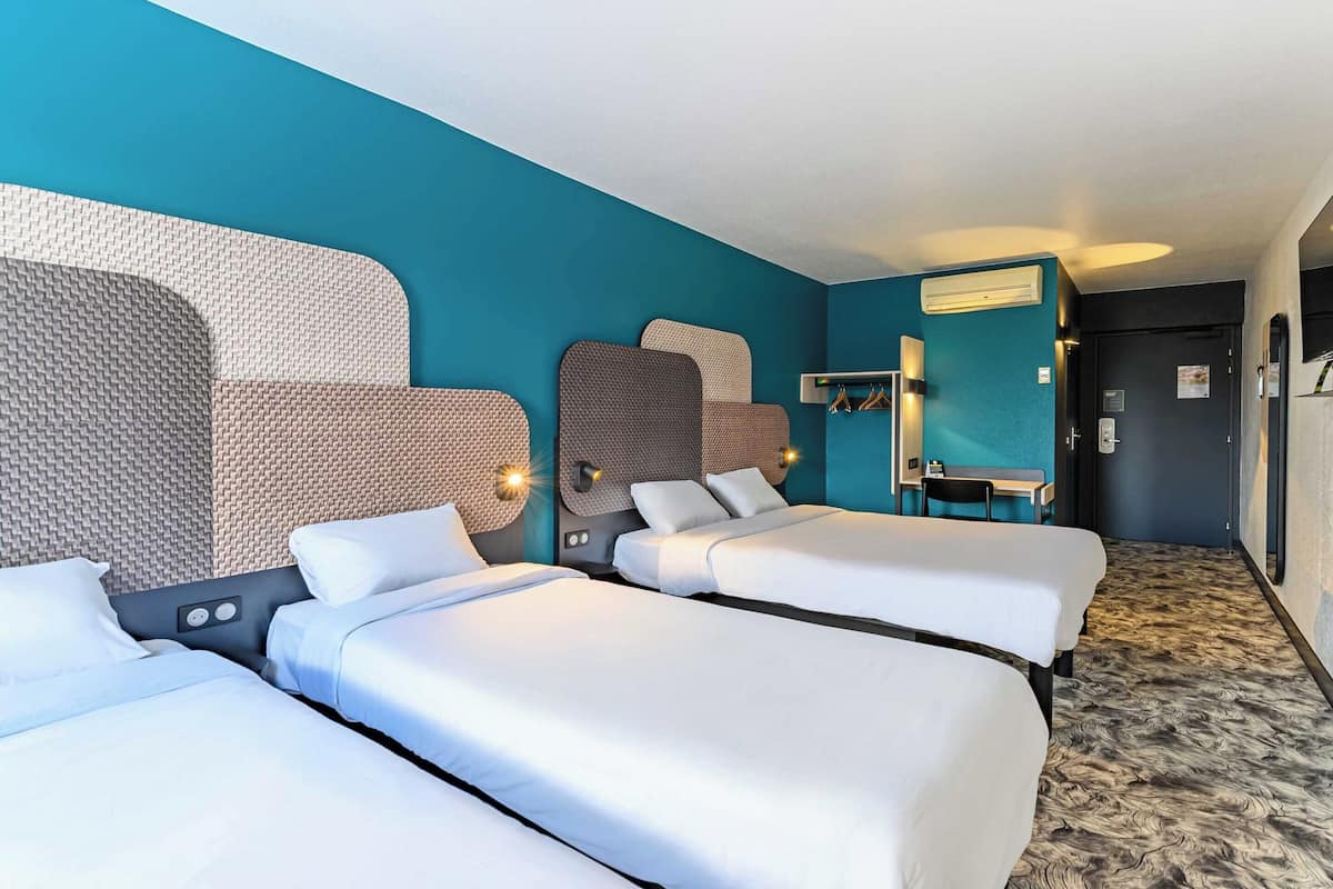 Una habitación de hotel con tres camas, un espejo grande y un armario con ropa colgada.