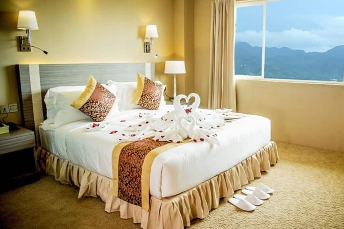 Habitación de hotel con una cama grande, dos lámparas de noche, una mesita de noche y vistas a las montañas desde la ventana.
