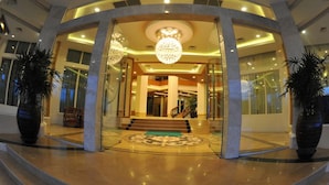 A grand entrance with a large chandelier, a staircase leading to the upper floor, and potted plants on either side. - Hotel Hazel (Mandalay)