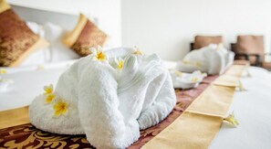 A neatly made bed with a white towel and a yellow flower, a brown pillow, and a brown headboard. - Hotel Hazel (Mandalay)