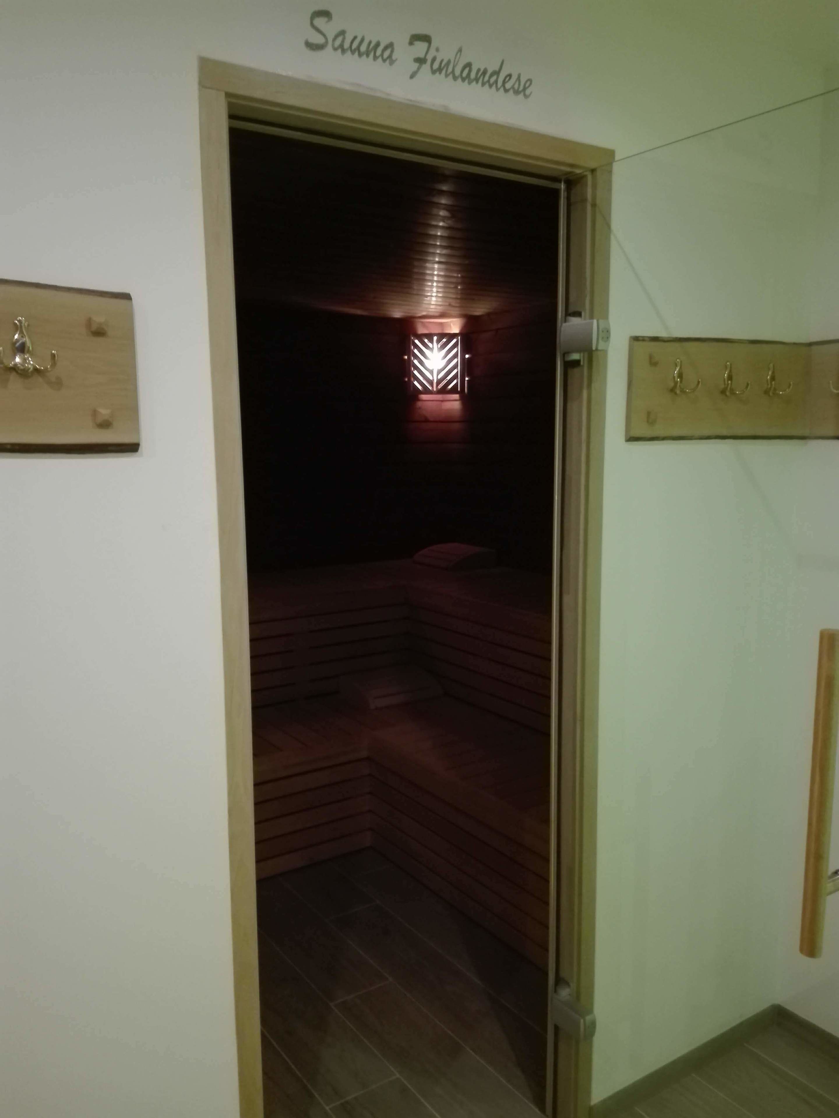 A sauna room with a wooden bench, a wall-mounted light fixture, and a sign reading "Sauna Finlandese".