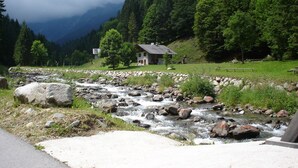 Una casa junto al río con muro de piedra y mesas de picnic.
