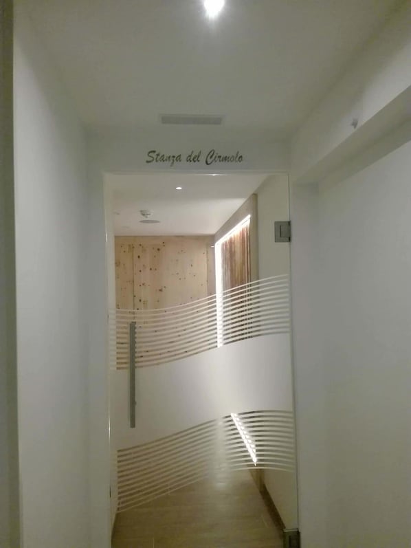 A hallway with a wooden floor, white walls, and a ceiling with recessed lighting. - Hotel Denny (Carisolo)