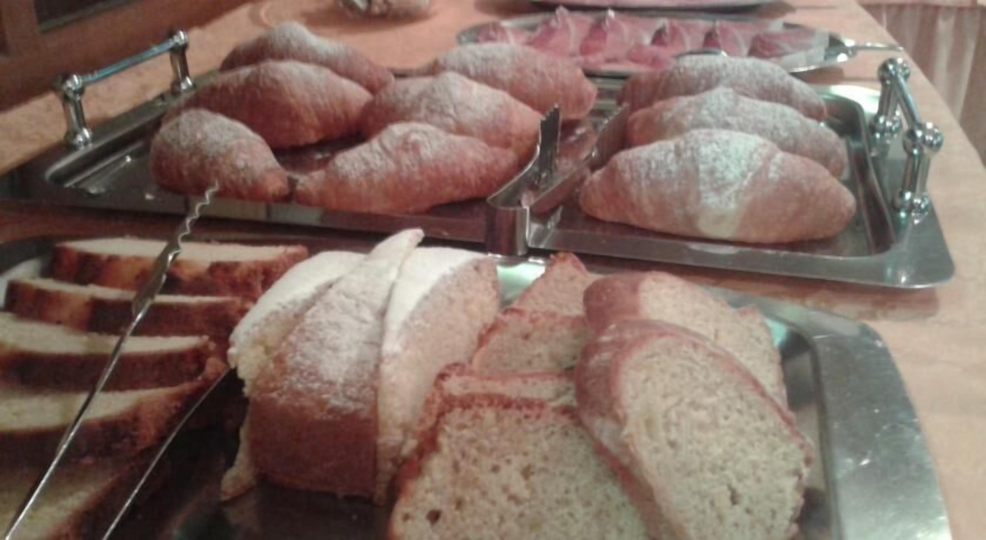 A buffet with various breads and pastries on trays.