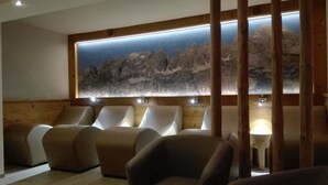 Una habitación con una obra de arte grande colgada en la pared que representa un paisaje montañoso, varias zonas de estar con cojines y un diseño de paneles de madera.