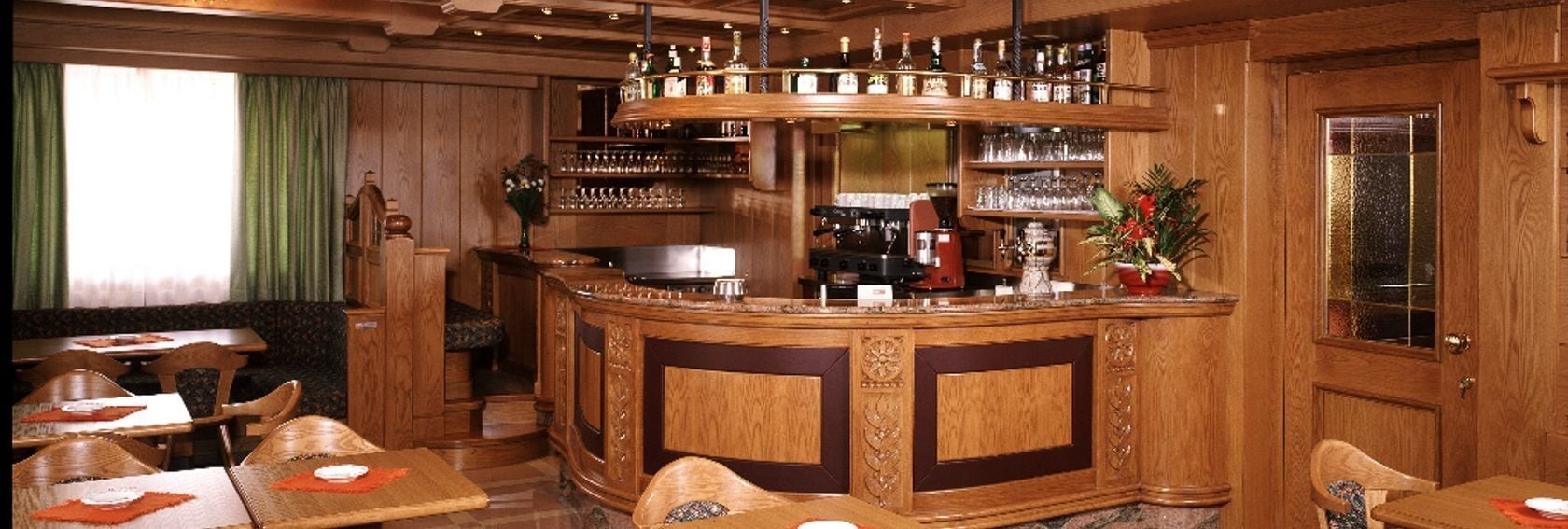 Een bar met houten meubels, een koffieapparaat en diverse flessen en glazen op planken.