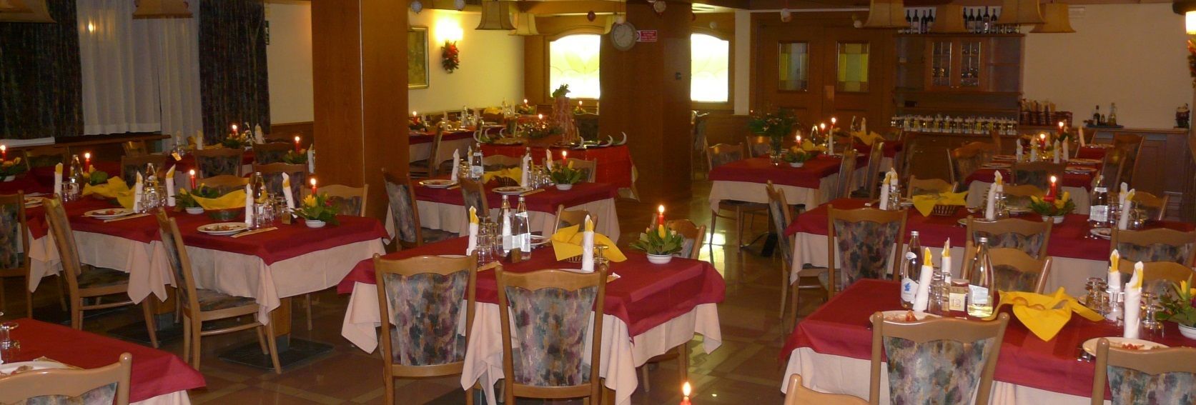 Een restaurant met meerdere tafels gedekt voor diners, elk met een rode tafelkleed en kaarsen.