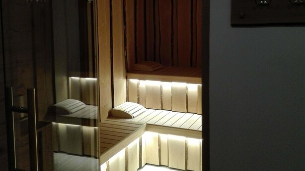 Una habitación con poca luz, un banco de madera con listones y una cama pequeña.