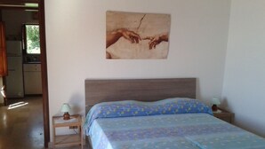 Un dormitorio con una cama, dos mesitas de noche con lámparas, un cuadro en la pared y vistas a una cocina.