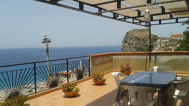Una terraza con vistas al mar, plantas en macetas y una mesa con sillas.