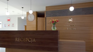 Un mostrador de recepción de hotel con detalles de madera, un reloj y un florero con flores.