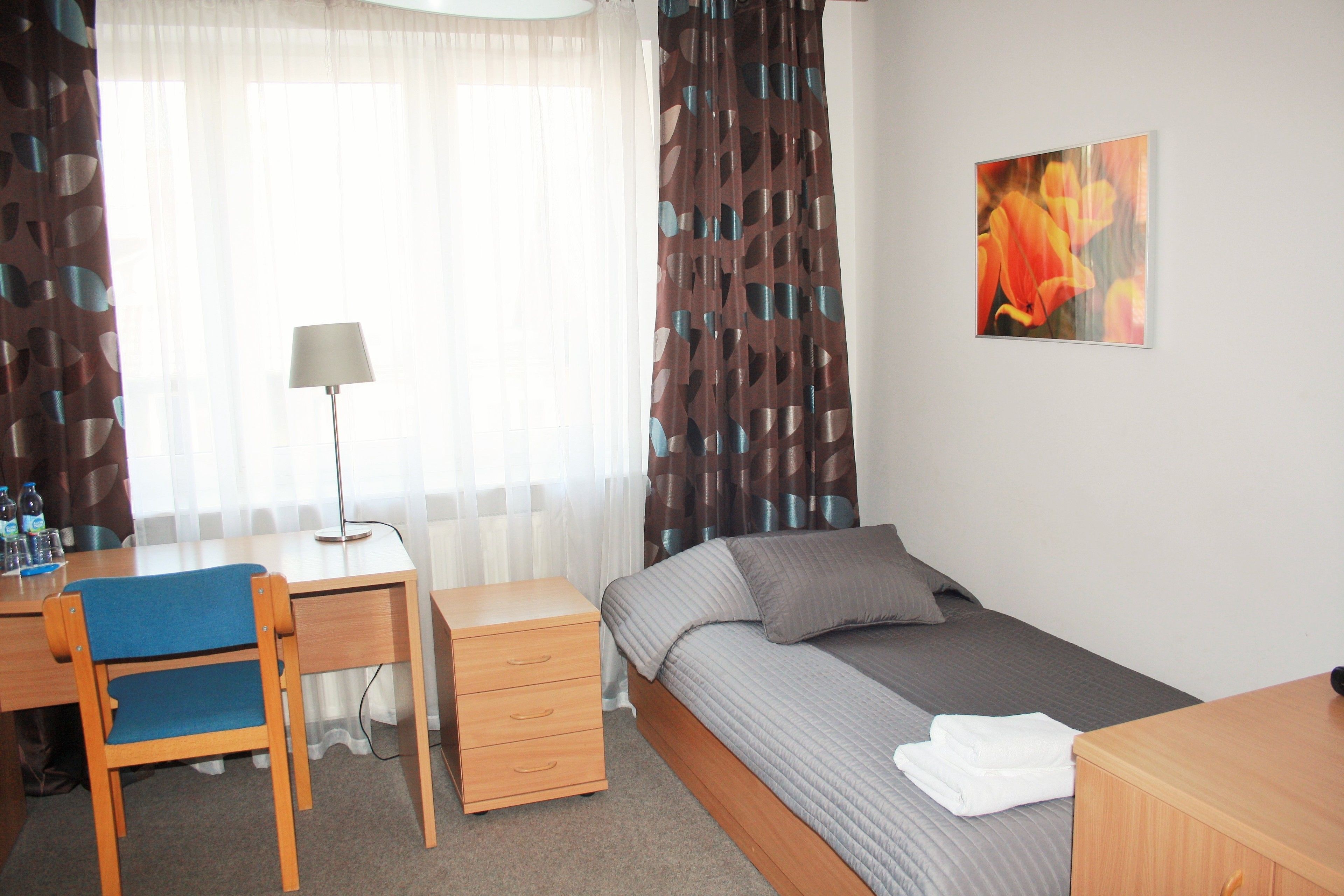 A hotel room with a bed, a desk with a chair, a lamp, and a painting on the wall.