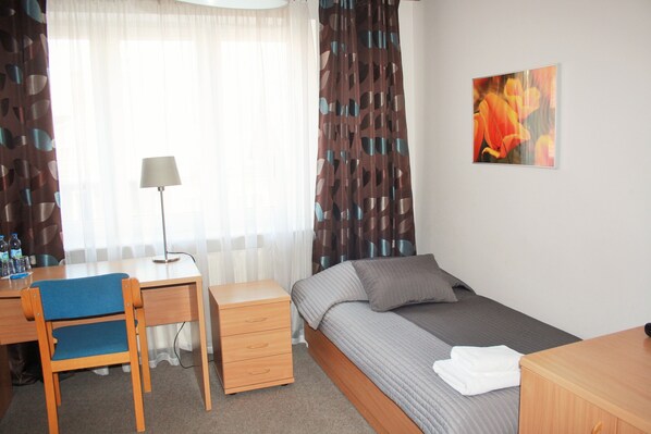 Una habitación de hotel con una cama, un escritorio con silla, una lámpara y un cuadro en la pared.