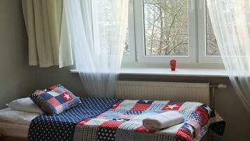 A single bed with a quilt, a window with curtains, and a radiator.