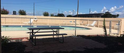 A fenced pool area with a picnic table, lounge chairs, and a clear blue sky.
