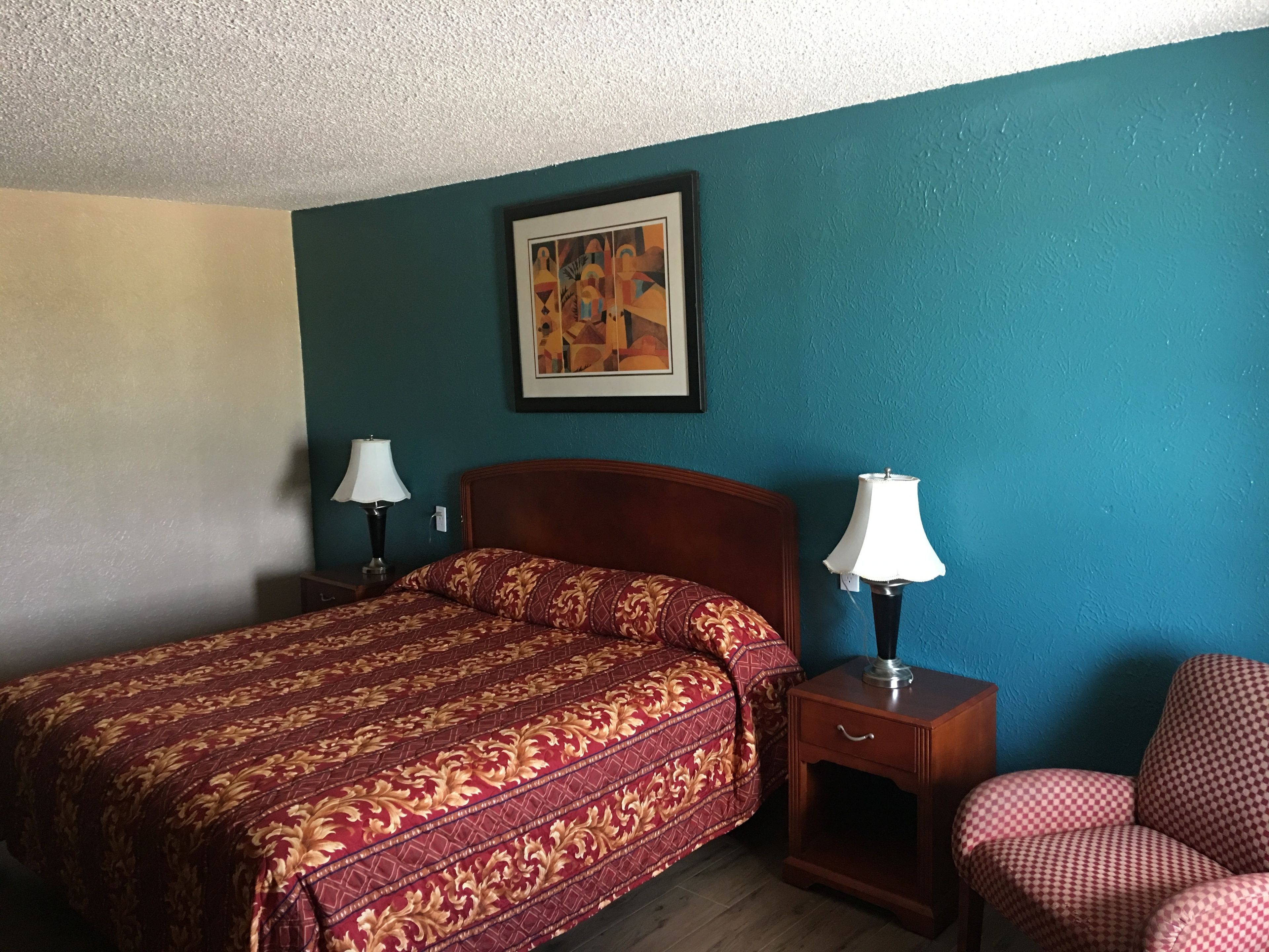 A hotel room with a bed, two bedside tables with lamps, a chair, and a painting on the wall.