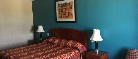 Une chambre d’hôtel avec un lit, deux tables de chevet avec des lampes, une chaise et un tableau au mur.