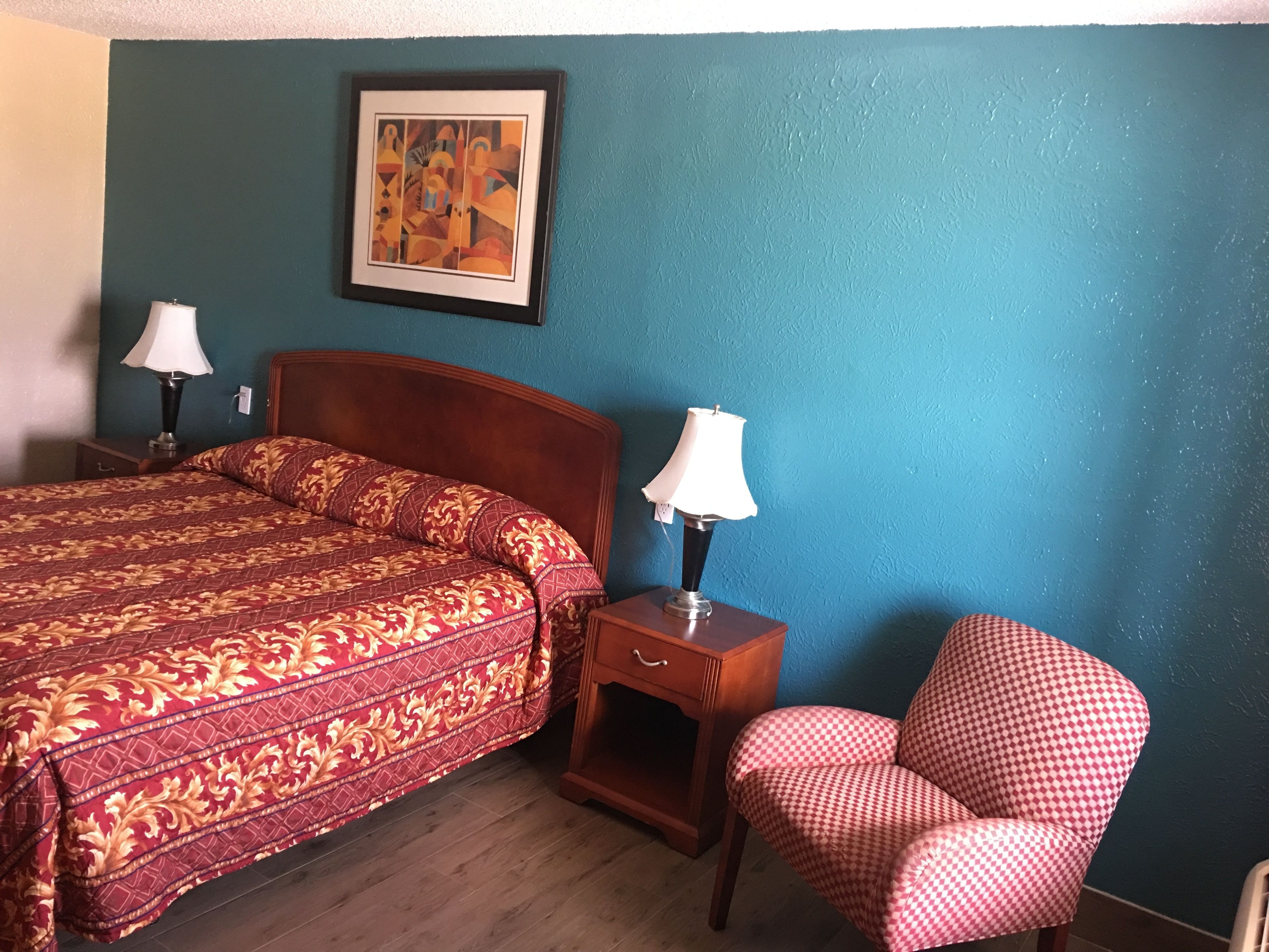 A bedroom with a bed, two bedside lamps, a chair, a nightstand, and a framed artwork on the wall.