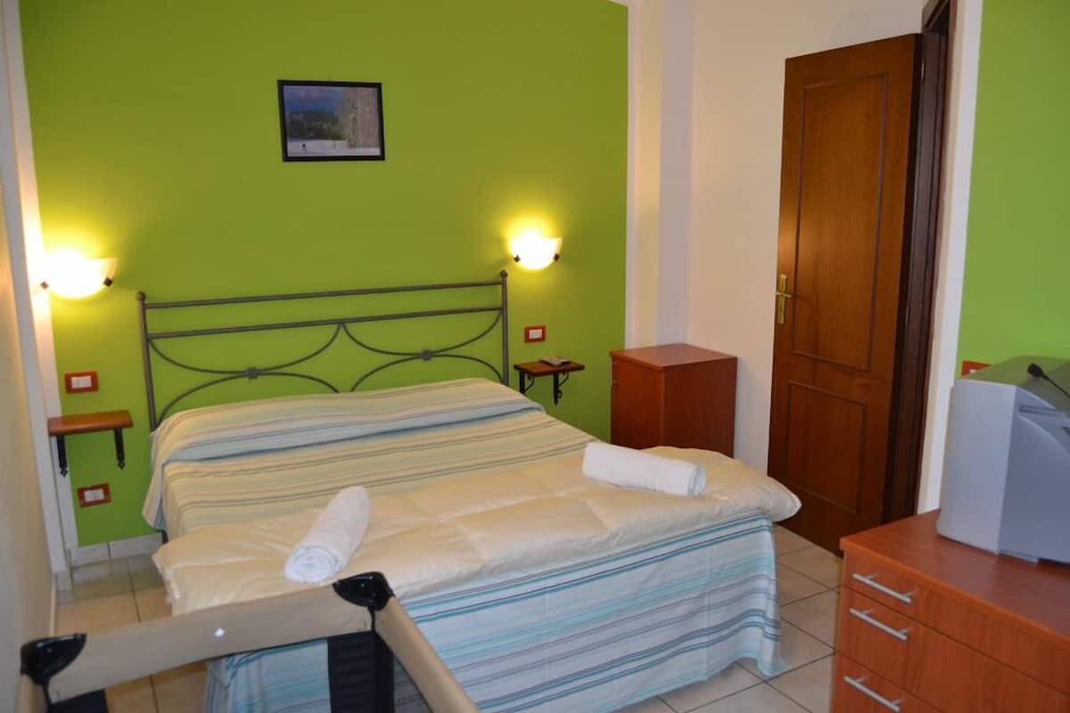 A neatly made bed with striped bedding, two bedside tables with lamps, a wooden wardrobe, and a door.