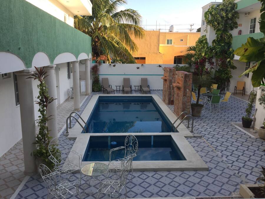 A rooftop pool area with a rectangular pool, surrounded by lounge chairs and tables.