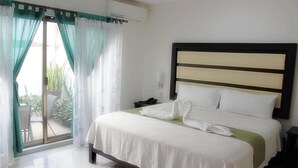 Habitación de hotel con cama, mesita de noche, ventana con cortinas y vistas al exterior.
