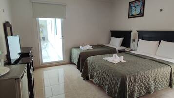 A hotel room with two beds, a desk, a chair, a television, and a ceiling fan.