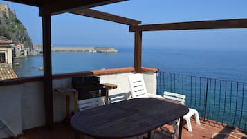 A terrace with a table and chairs, overlooking a coastal area with a sea view and a rocky cliff.