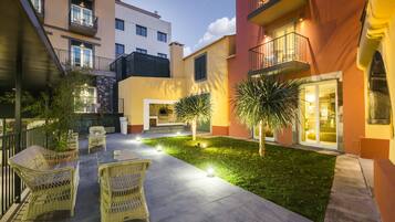 Un patio con mobiliario exterior, un pequeño césped y un edificio con balcones.