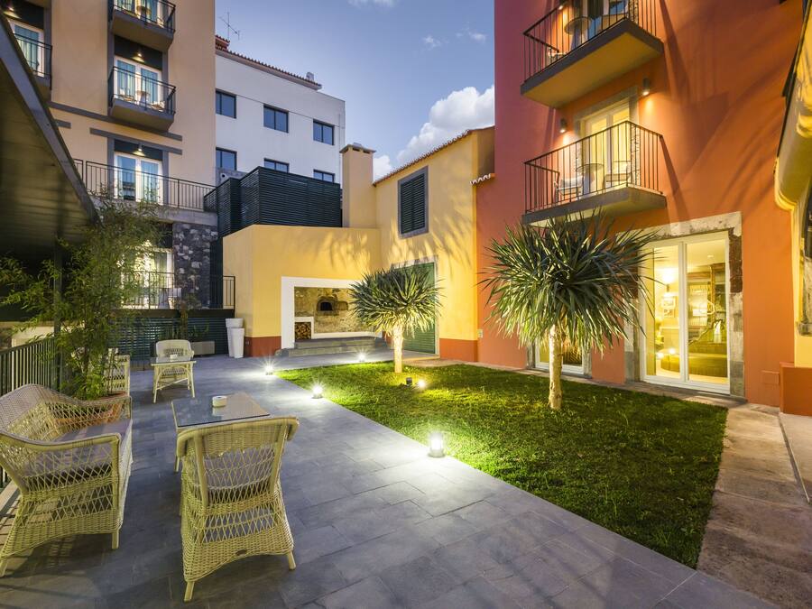 Un patio con mobiliario exterior, un pequeño césped y un edificio con balcones.