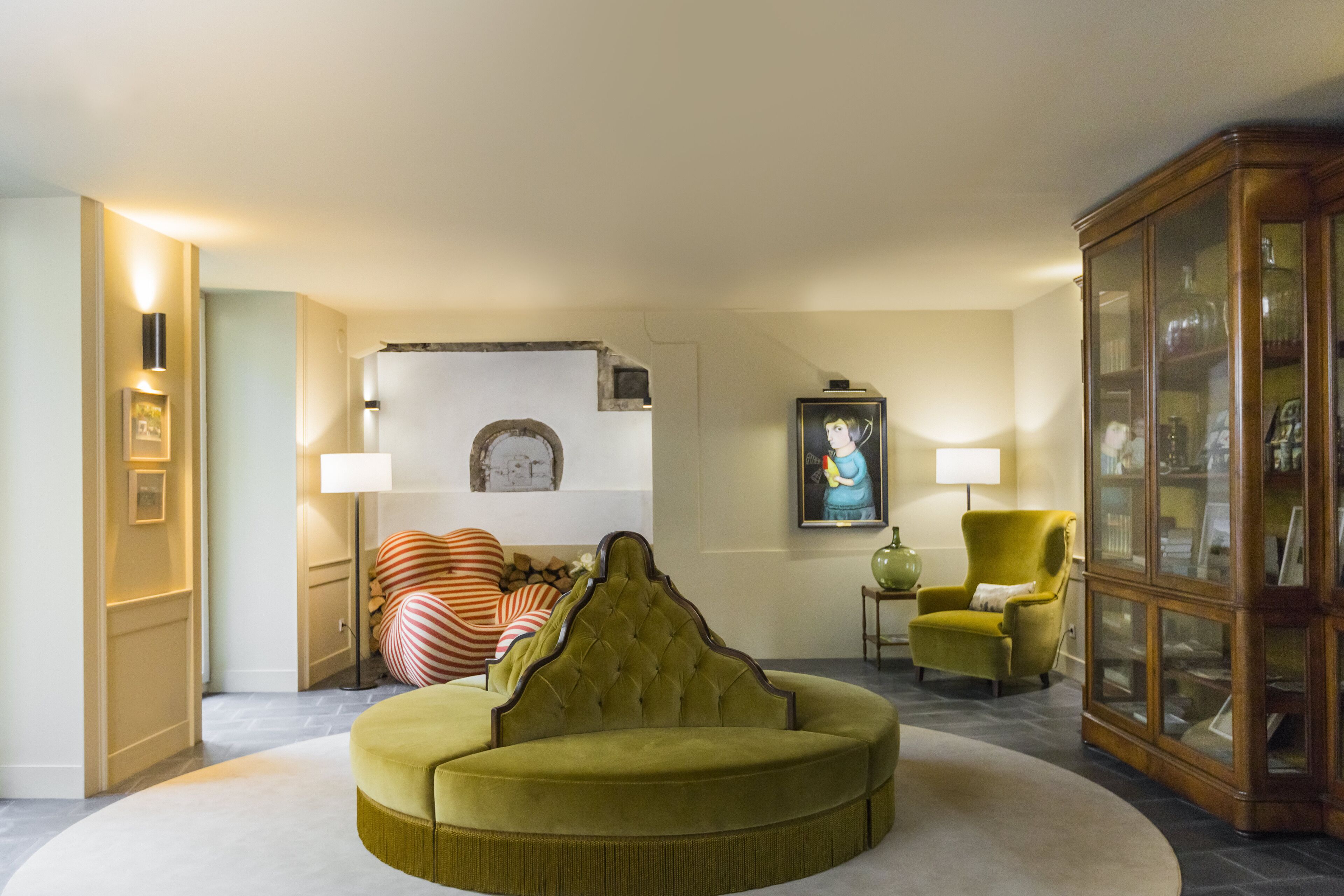 A circular green sofa in a well-lit living room with a glass cabinet and a yellow armchair.