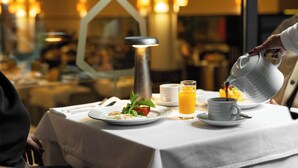 En frukostuppdukning med ett bord för två personer, inklusive tallrikar med mat, en kopp kaffe och ett glas apelsinjuice.