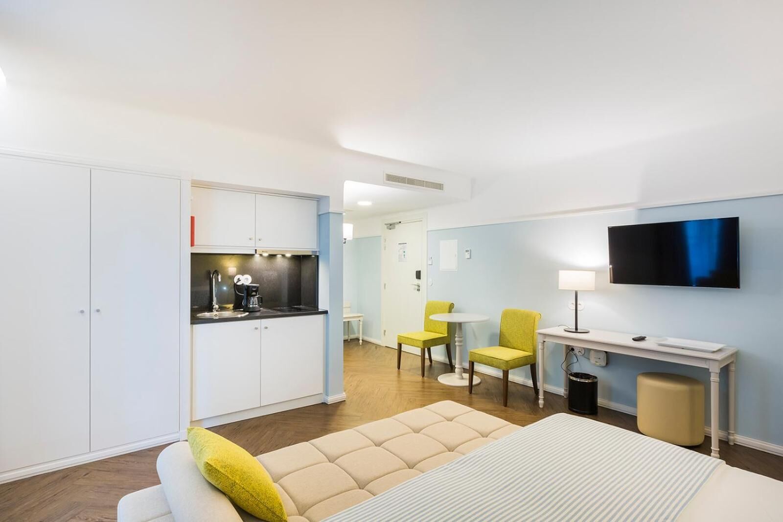 Une chambre d’hôtel compacte comprenant un coin cuisine, un lit, un espace salon avec des chaises, une télévision et une petite table.
