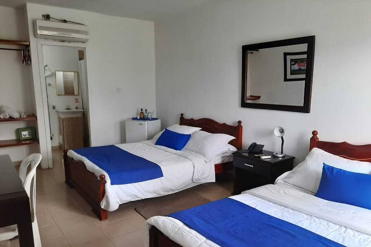 A hotel room with two beds, a desk, a chair, a wardrobe, and a mirror on the wall.