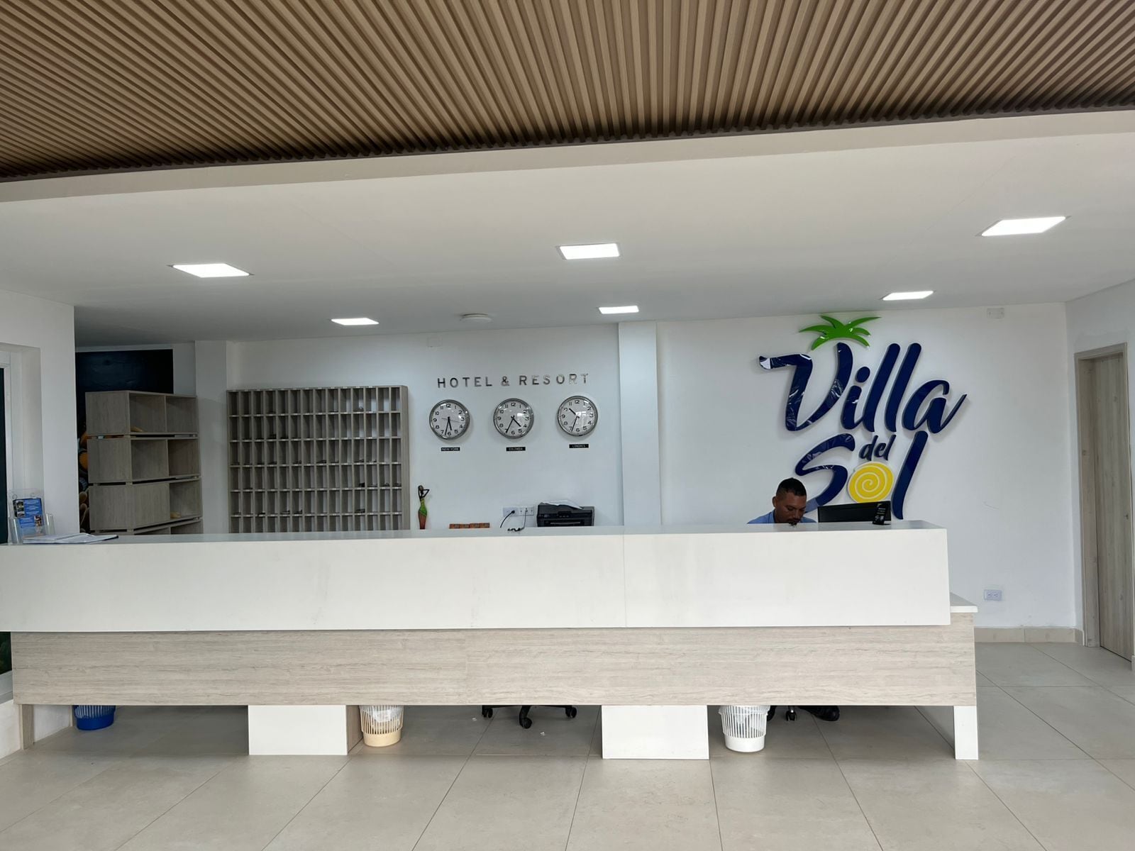 Uma receção de hotel com design moderno, um relógio e uma placa com a inscrição 'Villa del Sol'.