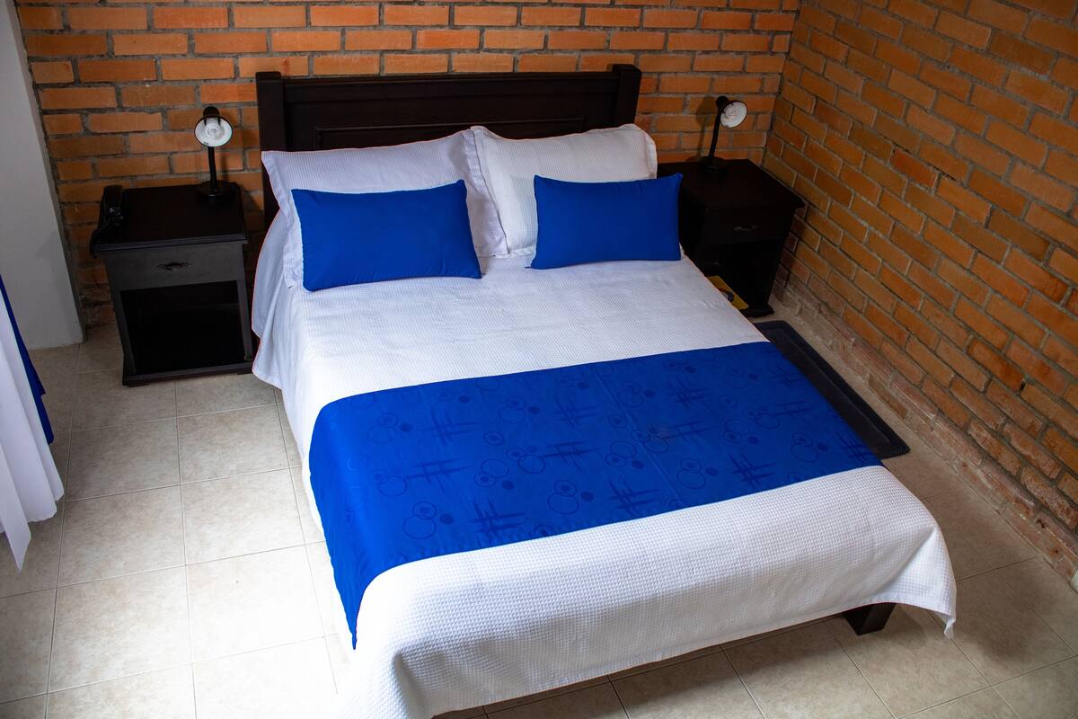A neatly made bed with a blue and white bedspread, two bedside tables with lamps, and a brick wall background.