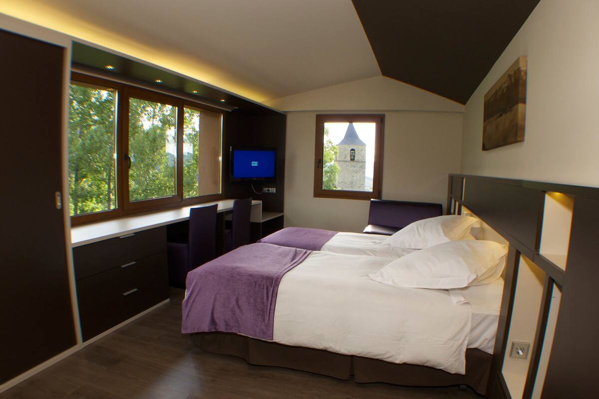 A bedroom with a bed, a desk, and a TV.