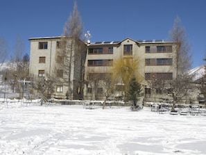 A multi-story building with a stone facade, multiple windows, and a flat roof with solar panels. - Hotel Mirador (Lles)