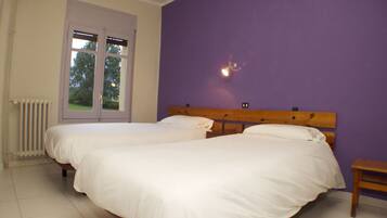 A bedroom with two beds, a window, and a radiator.