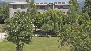 A stone building with a tiled roof, surrounded by lush greenery and trees. - Hotel Mirador (Lles)